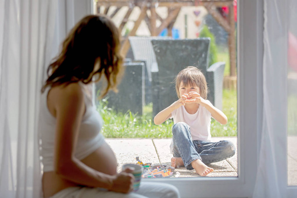 Young pregnant woman, sitting indoor, watching her child through - Foto, afbeelding