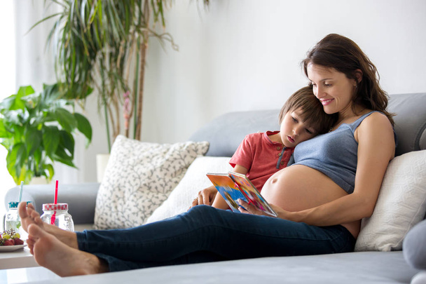 Young pregnant woman, reading a book at home to her boy - Photo, image