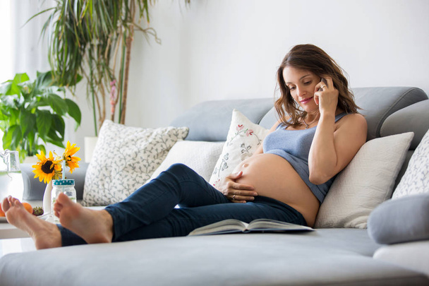 Young pretty pregnant woman speaking on the phone at home on the - Фото, изображение