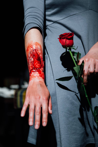 girl with a red rose shows the public the final work of the make-up artist: a wound or burned. - Foto, Imagem