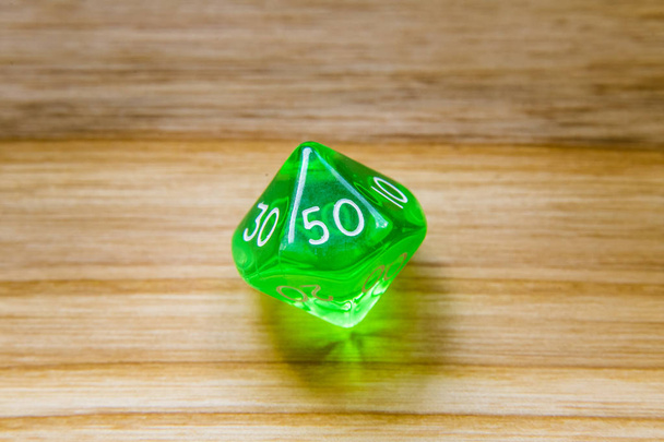 Полупрозрачный зеленый с десятью сторонами играя в кости на деревянной спинке
 - Фото, изображение