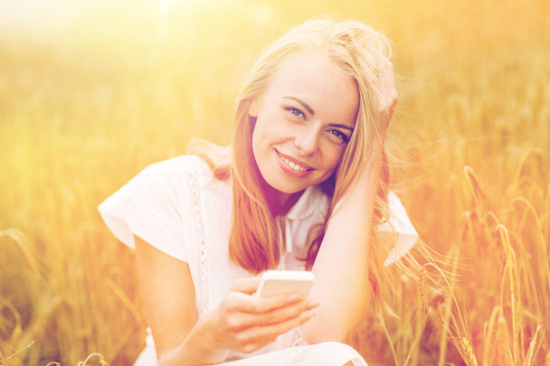 happy young woman with smartphone on cereal field - 写真・画像