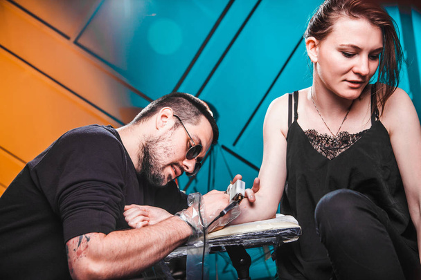 master tattooist makes a tattoo on the skin of the hand client girl in a workshop with special equipment - Foto, immagini