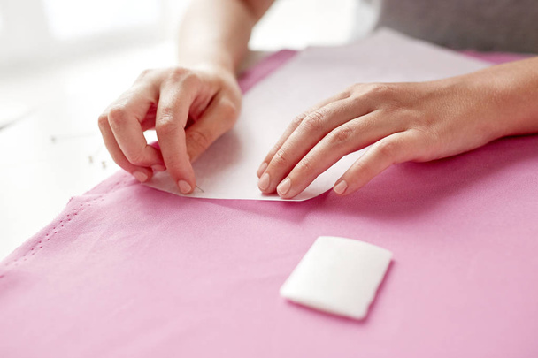woman with pins stitching paper pattern to fabric - Foto, Bild