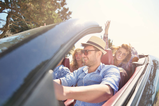 leisure, road trip, travel and people concept - happy friends driving in cabriolet car along country road - Foto, Bild