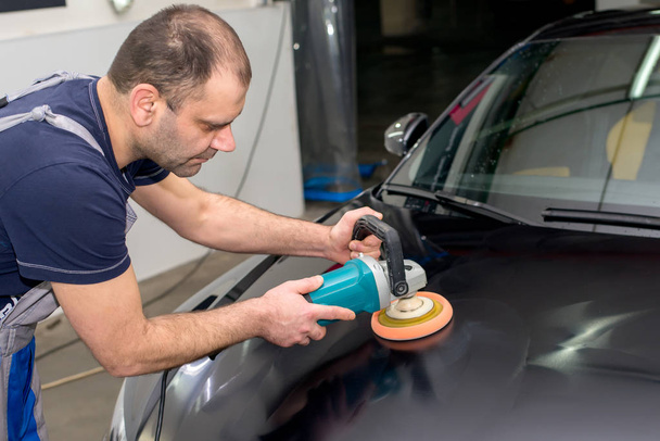 A man polishes a black car with a polishing machine - Valokuva, kuva