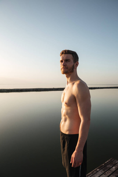 Portrait of a healthy shirtless sportsman standing outdoors with water - Foto, afbeelding