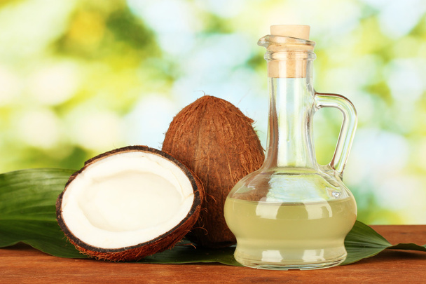 decanter with coconut oil and coconuts on green background - Фото, изображение