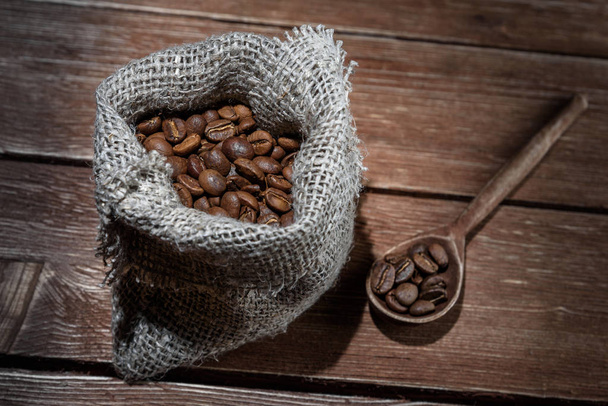 Coffee beans in hessian sack and scoop on a brown wooden background - Zdjęcie, obraz