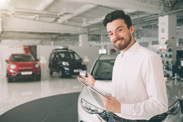 friendly vehicle salesman presenting new cars at showroom. Photo of young male consultant showing new car in auto show. Concept for car rental - Foto, immagini