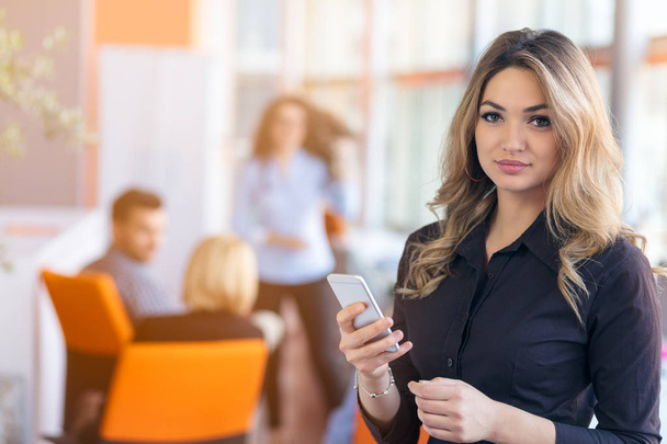 Portrait of young businesswoman in office holding her mobile - Foto, afbeelding