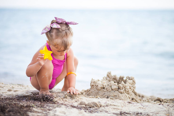 Μικρό κορίτσι στην παραλία κτίριο ένα κάστρο φτιαγμένο από άμμο - Φωτογραφία, εικόνα