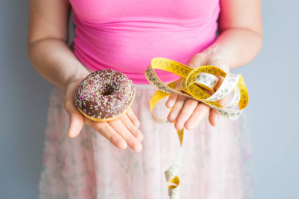 Κοντινό πλάνο γυναικεία χέρια κρατώντας ένα ντόνατ και μία μεζούρα. Η έννοια της υγιεινής διατροφής. Διατροφή. - Φωτογραφία, εικόνα