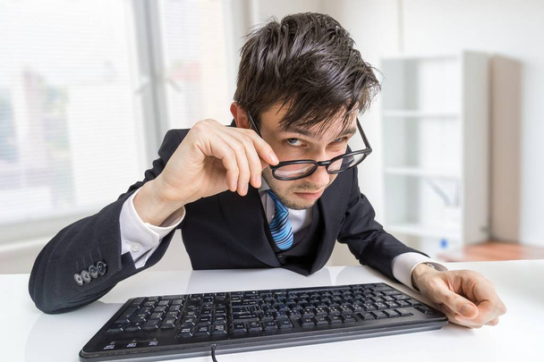 Ύποπτες άνθρωπος γυαλιά εργάζεται σε γραφείο και ψάχνει στο yo - Φωτογραφία, εικόνα