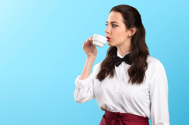 Young beautiful waitress holding a cup of coffee on colorful background - Photo, Image