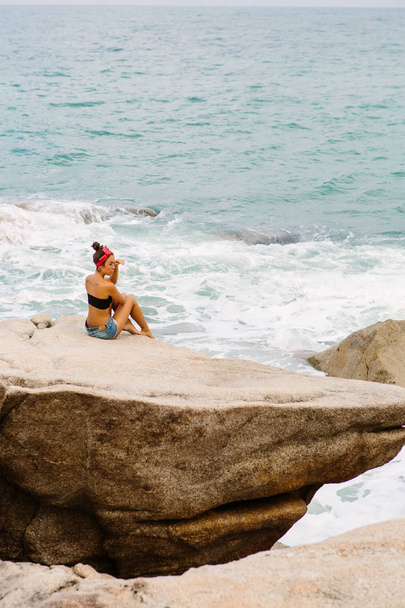 Beautiful girl in short shorts sit on big stones. - Foto, afbeelding