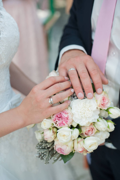 Manos con anillos en un fondo de ramo de boda
 - Foto, imagen