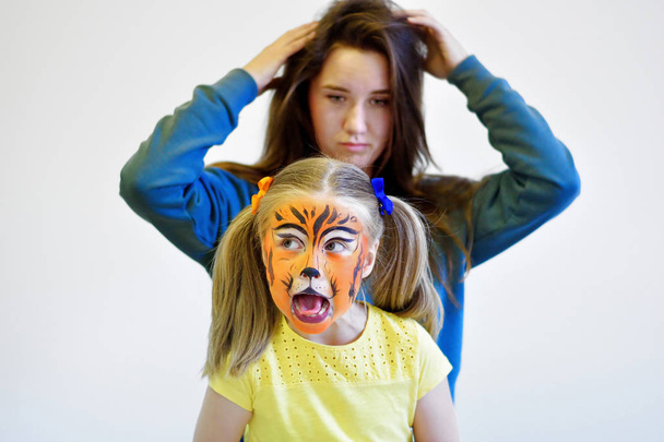 Screaming girl with painted tiger face and her mother - Fotó, kép