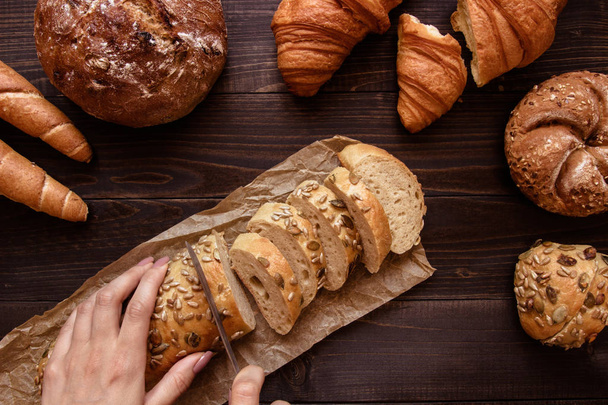 Hands slicing fresh bread on the dark wooden background top view - Foto, imagen