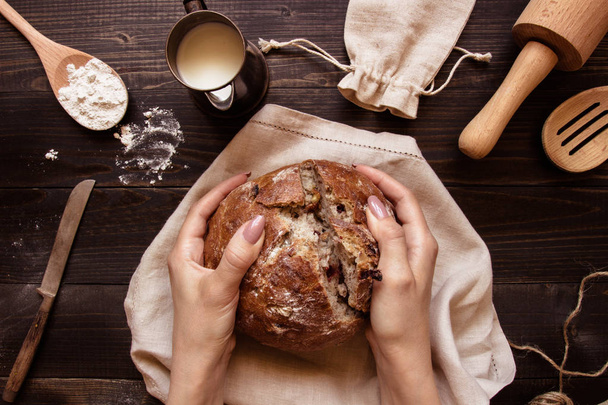 Hands holding fresh homemade bread on the dark wooden background top view - Foto, Imagen