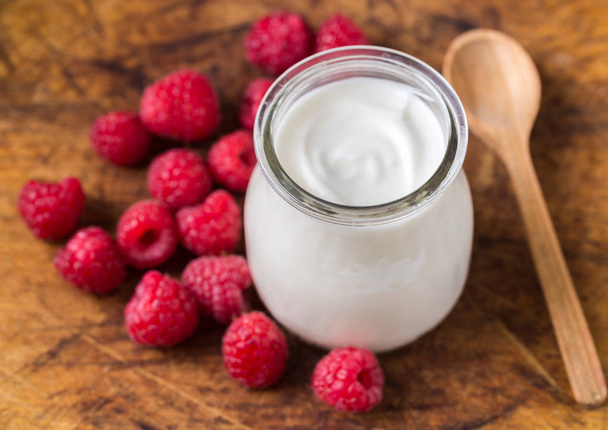 Yogurt bianco con lamponi in ciotola di vetro su tavolo rustico
. - Foto, immagini