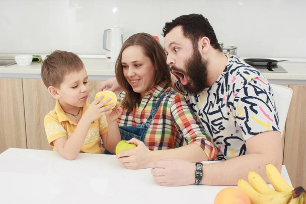 family of three eating fruits in the kitchen, family in the kitchen, - Фото, изображение