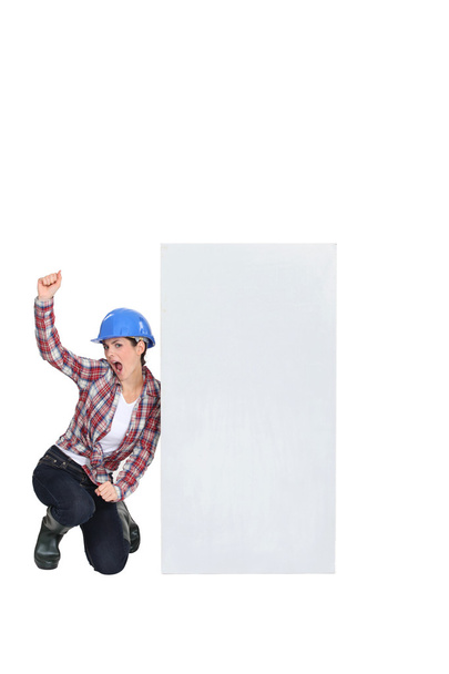 Excited female builder kneeling by blank poster - Foto, afbeelding
