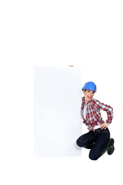 Female builder kneeling by blank poster - Фото, изображение