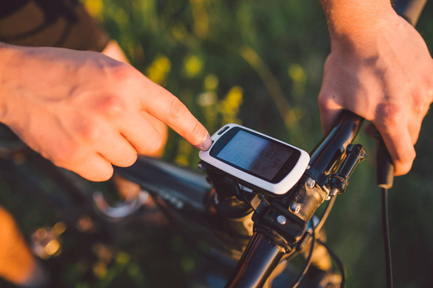 A young brunette guy on a mountain bike uses a cycling computer, a navigator in the field sunset of the day - Foto, imagen