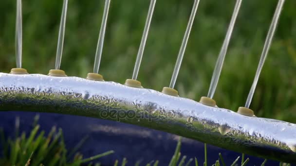 Gazon sprinklersysteem op tuin in gras. Strooi spuit water op het gras in de tuin op een achtergrond van bomen als de zon schijnt - Video