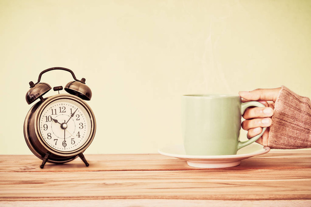 mano sosteniendo una taza de café y reloj despertador en la mesa de madera, c
 - Foto, Imagen