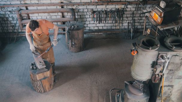 Σιδεράς άνθρωπος γένια σε σφυρηλατήσει κάνει μεταλλικά εργαλεία στο αμόνι σιδερένια με σφυρί, το top view - Φωτογραφία, εικόνα