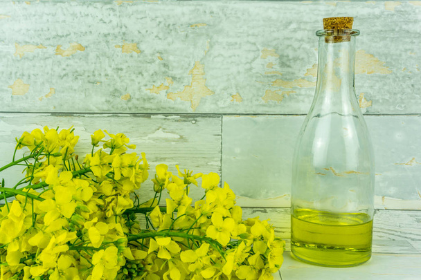 Rapeseed flowers with a bottle of rapeseed oil on a rustic wooden table - Foto, imagen