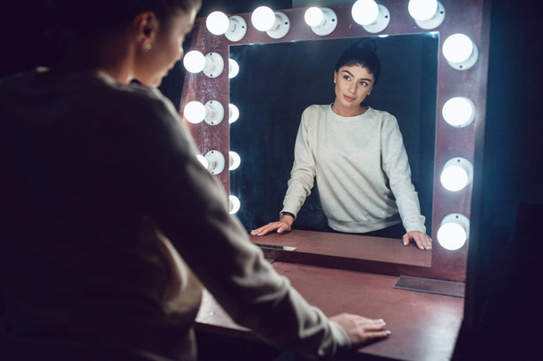 Attractive brunette in a gray sweatshirt looks in the mirror. - Valokuva, kuva