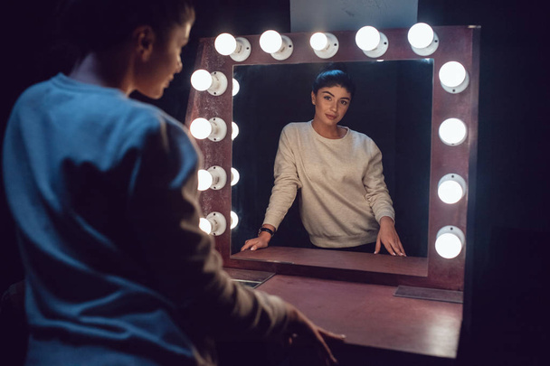 Attractive brunette in a gray sweatshirt looks in the mirror. - Фото, зображення