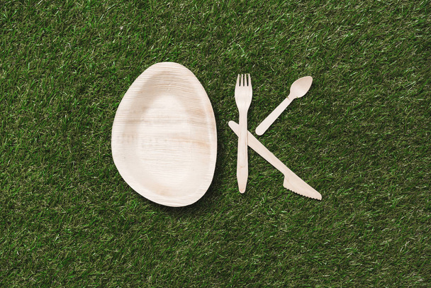 wooden cutlery items and plate on grass - Foto, afbeelding