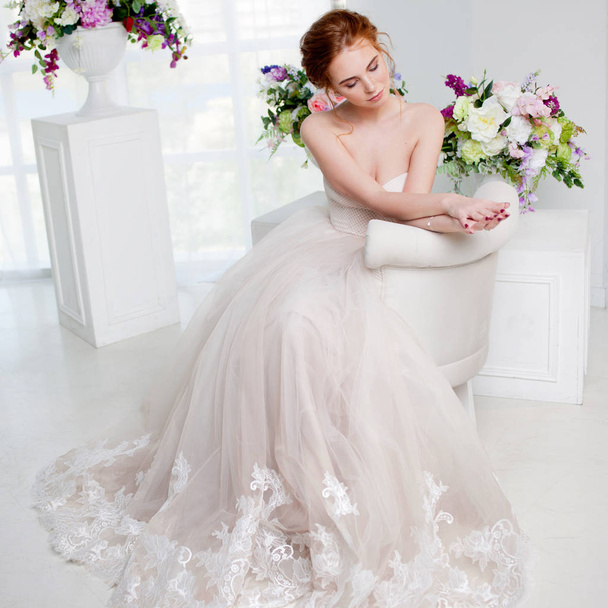 Portrait of a beautiful girl in a wedding dress. Bride in luxurious dress sitting on a chair - Foto, afbeelding