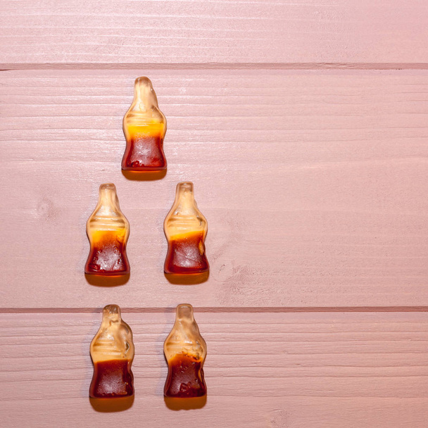 Cola garrafas doces no fundo de madeira rosa silenciada. Cinco doces mastigáveis clássicos ou retrô dispostos em forma de garrafa. Culturas quadradas
 - Foto, Imagem