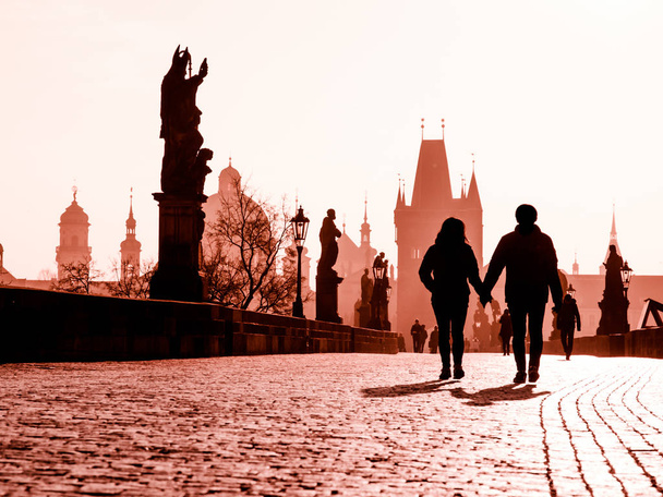 Foggy morning on Charles Bridge, Prague, Czech Republic. Sunrise with silhouettes of walking people, statues and Old Town towers. Romantic travel destionation - Photo, Image