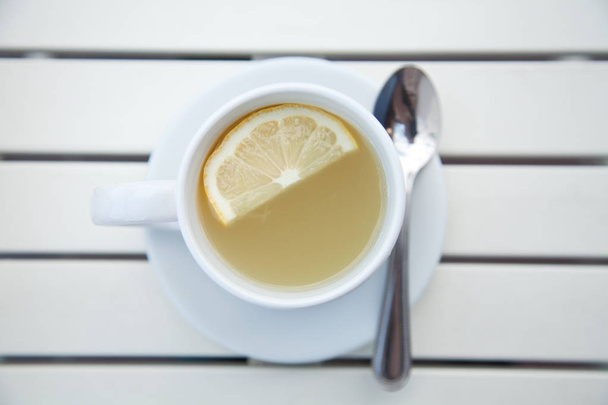 bílý šálek čaje zázvor citron s ploténkou a lžíci na bílý dřevěný stůl horní pohled - Fotografie, Obrázek