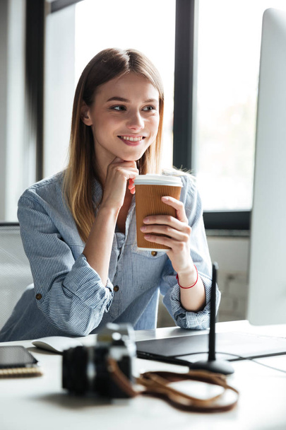 Smiling young woman work in office using computer drinking coffee. - Φωτογραφία, εικόνα