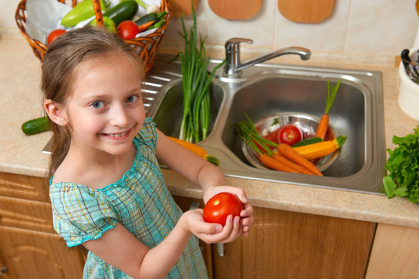 gyermek lány mosás zöldségek, friss gyümölcs, a konyha belső, egészséges élelmiszer koncepció - Fotó, kép