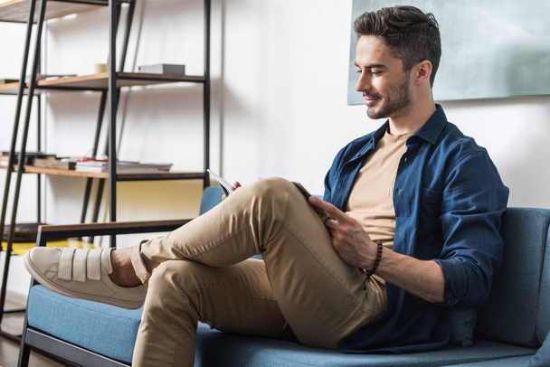 Cheery youthful bearded guy spending spare time inside apartment - Photo, Image