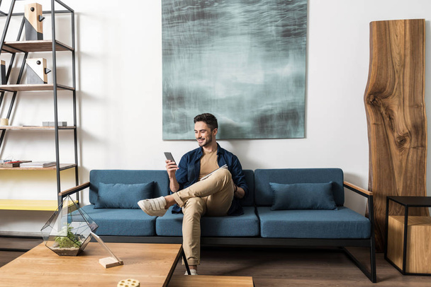 Happy youthful guy bearded resting with cellphone in living room - Fotoğraf, Görsel