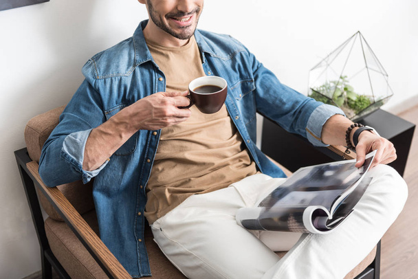 Cheery youthful guy resting with mug of hot beverage indoor - Photo, image