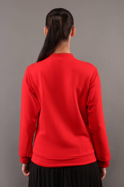 Costas de menina jovem hipster vestindo camisola de algodão vermelho em branco com espaço de cópia para o seu design ou logotipo, mock-up de ltemplate mulheres com capuz, parede cinza no fundo
 - Foto, Imagem