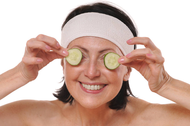 Cheerful mature woman holding pieces of cucumber in front of her eyes - Fotó, kép