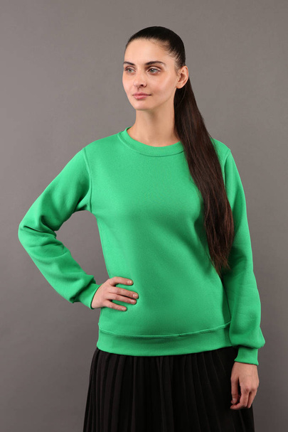 Young hipster girl wearing blank lime green cotton sweatshirt with copy space for your design or logo, mock-up of ltemplate womens hoodie, grey wall in the background - Foto, afbeelding