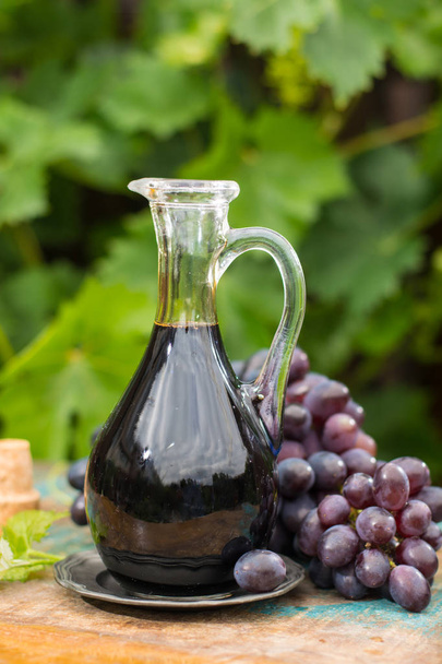 Black old balsamic vinegar in a glass jug with fresh red grapes  - Photo, image