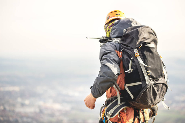 Close-up of a climber from the back in gear and with a backpack with equipment on the belt, stands on a rock, at high altitude - Фото, изображение